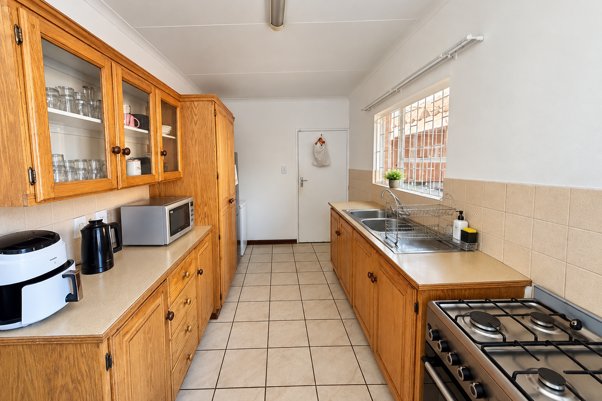 A functional galley-style kitchen featuring traditional wooden cabinetry, laminate countertops, a gas hob, and tiled flooring with ample storage space.