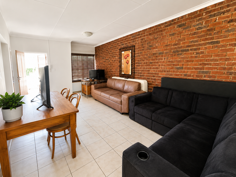 Spacious living area featuring a prominent exposed brick wall, neutral ceramic floor tiles, and natural light through a window with venetian blinds.