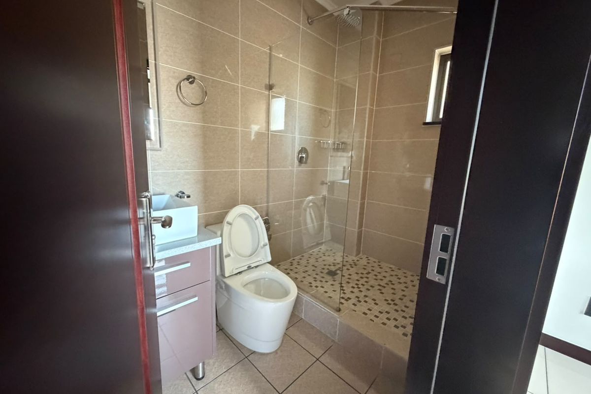 A modern bathroom featuring a walk-in shower with a glass screen, wall-mounted toilet, and a vanity cabinet with neutral wall and floor tiling.