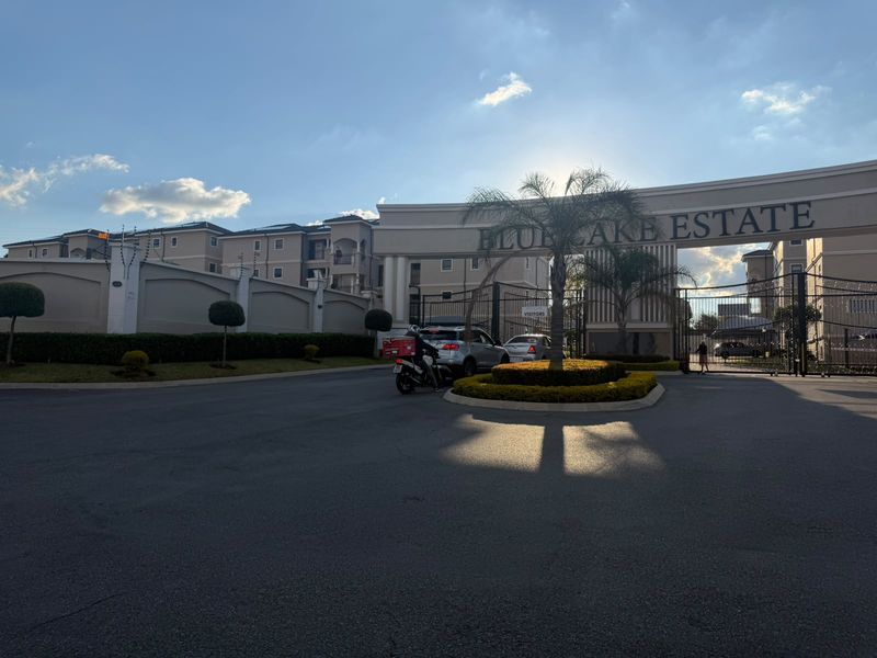 The entrance to Blue Lake Estate featuring a secure gated access point, perimeter walling with electric fencing, and well-maintained landscaped grounds.