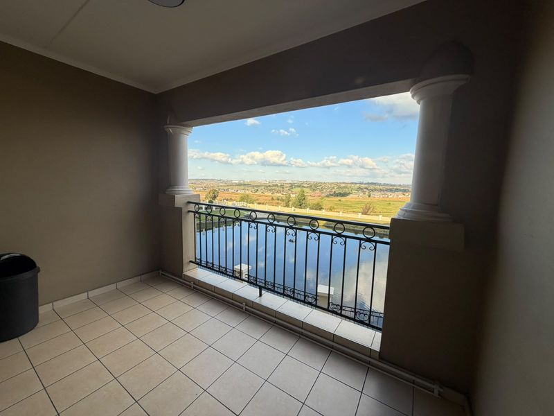 A spacious covered balcony featuring tiled flooring, decorative columns, and a wrought iron balustrade, offering expansive scenic views.