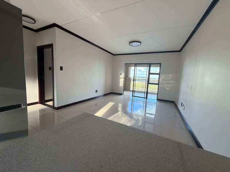 An open-plan living area featuring tiled flooring, a stone countertop, and a sliding glass door leading to a balcony with scenic views.