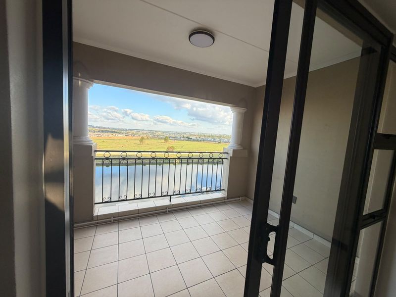 A covered balcony featuring tiled flooring, decorative columns, and a wrought iron balustrade, offering expansive views of the surrounding landscape and water.