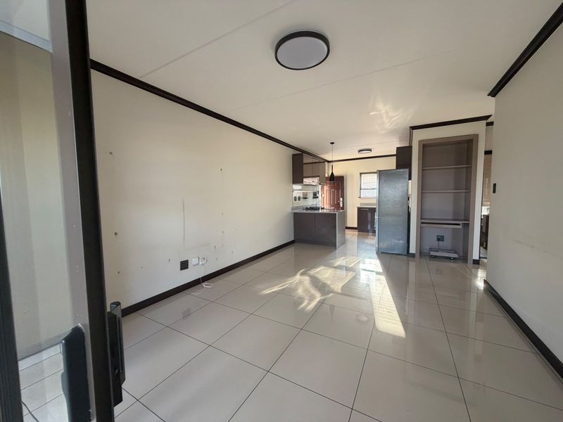 An open-plan living and kitchen area featuring tiled flooring, built-in cabinetry, and a dedicated shelving unit, offering a bright and versatile living space.