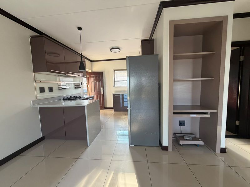 Modern kitchen featuring high-gloss cabinetry, stone countertops, a gas hob, and integrated shelving, complemented by sleek tiled flooring throughout.