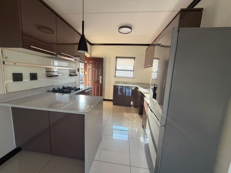 Modern kitchen featuring high-gloss cabinetry, stone countertops, a gas hob, and sleek tiled flooring, offering a clean and functional cooking space.