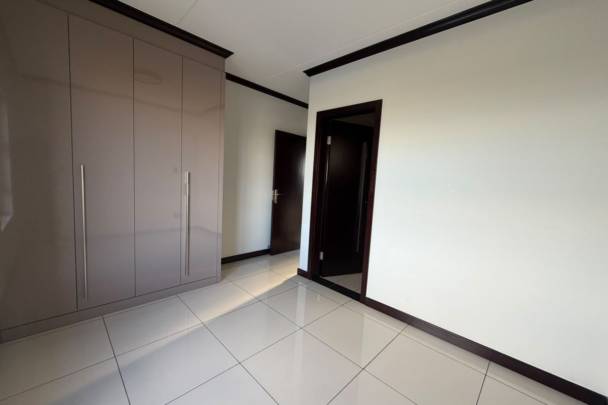 A clean, empty bedroom featuring modern high-gloss built-in cupboards, neutral tiled flooring, and dark wood door frames.