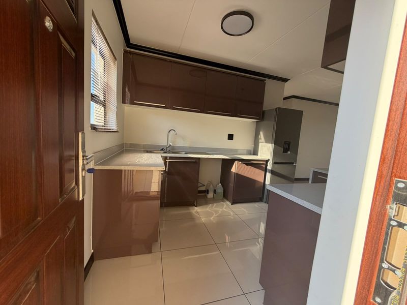 Modern kitchen featuring glossy brown cabinetry, stone-look countertops, stainless steel sink, and tiled flooring in a clean, open-plan layout.