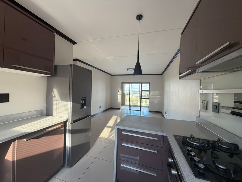 Modern open-plan kitchen and living area featuring sleek cabinetry, gas hob, stone countertops, and large sliding doors leading to a balcony with views.