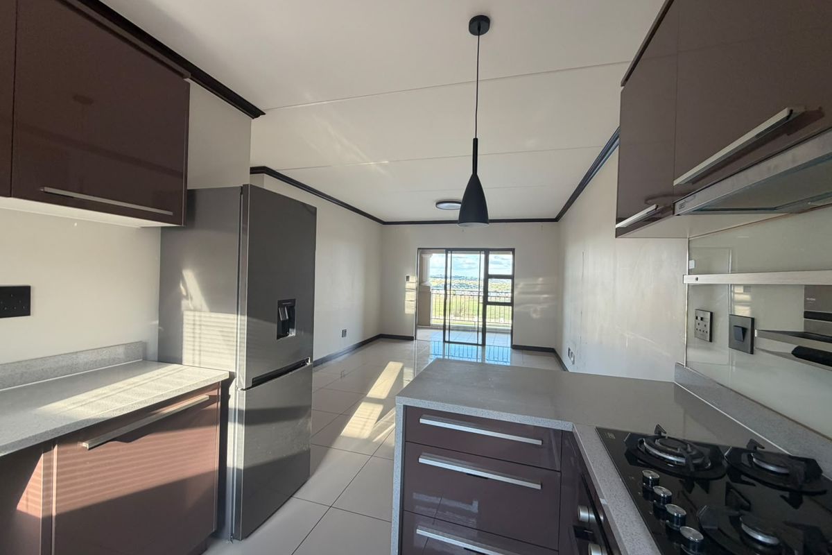 Modern open-plan kitchen and living area featuring sleek cabinetry, gas hob, stone countertops, and large sliding doors leading to a balcony with views.