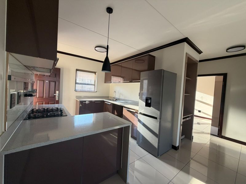 Modern kitchen featuring high-gloss cabinetry, stone countertops, gas hob, and tiled flooring, offering a clean and functional workspace.