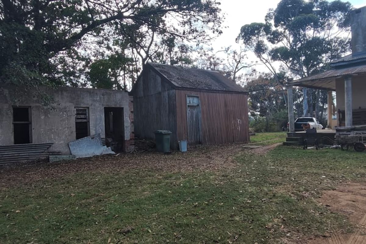 Rear yard view featuring a main house with veranda, a corrugated iron shed, and a secondary concrete outbuilding in need of significant maintenance.