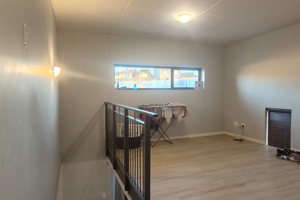 An open-plan mezzanine living area featuring light-toned laminate flooring, a modern metal balustrade, and neutral wall finishes.