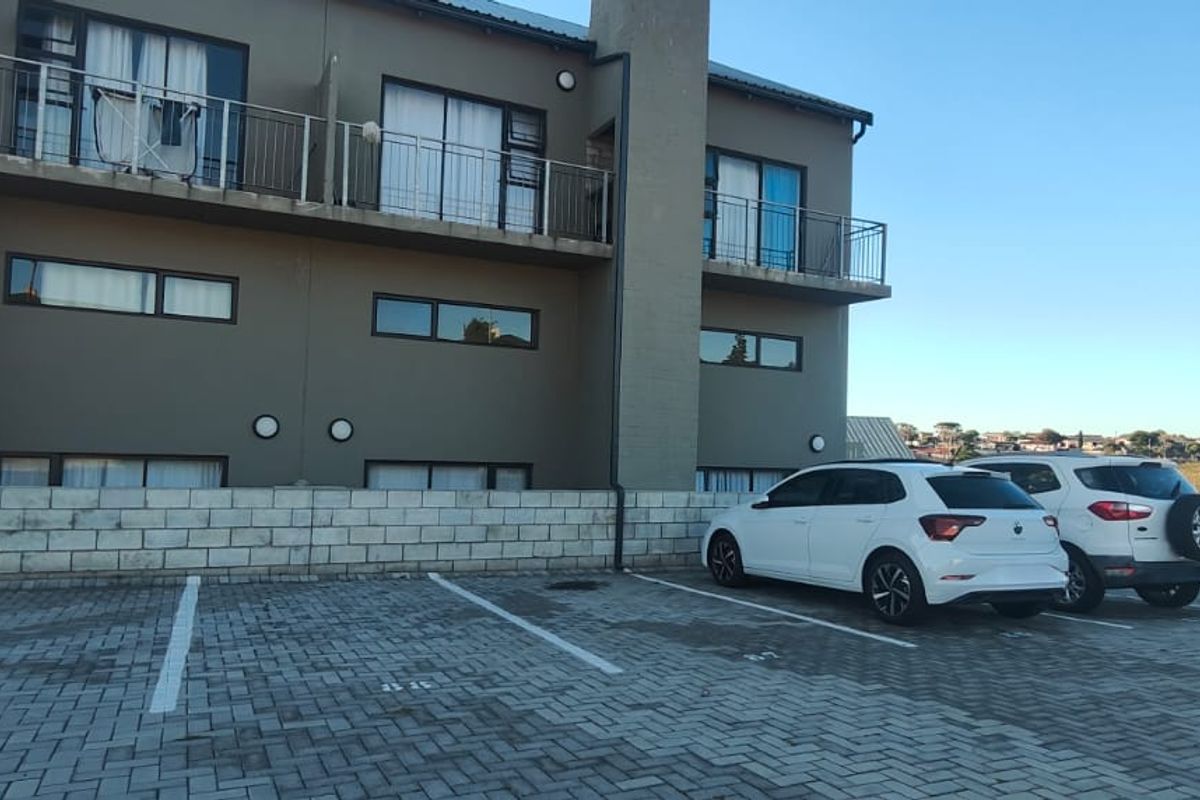 Rear view of the apartment complex featuring a paved parking area, ground floor access, and upper-level balconies with metal railings.