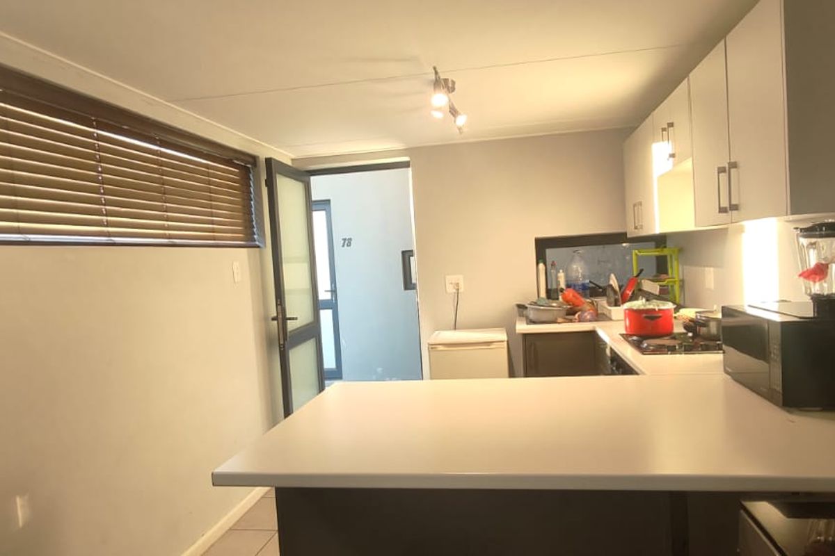 A functional kitchen featuring built-in cabinetry, a central island, and a hob, with natural light filtered through venetian blinds.