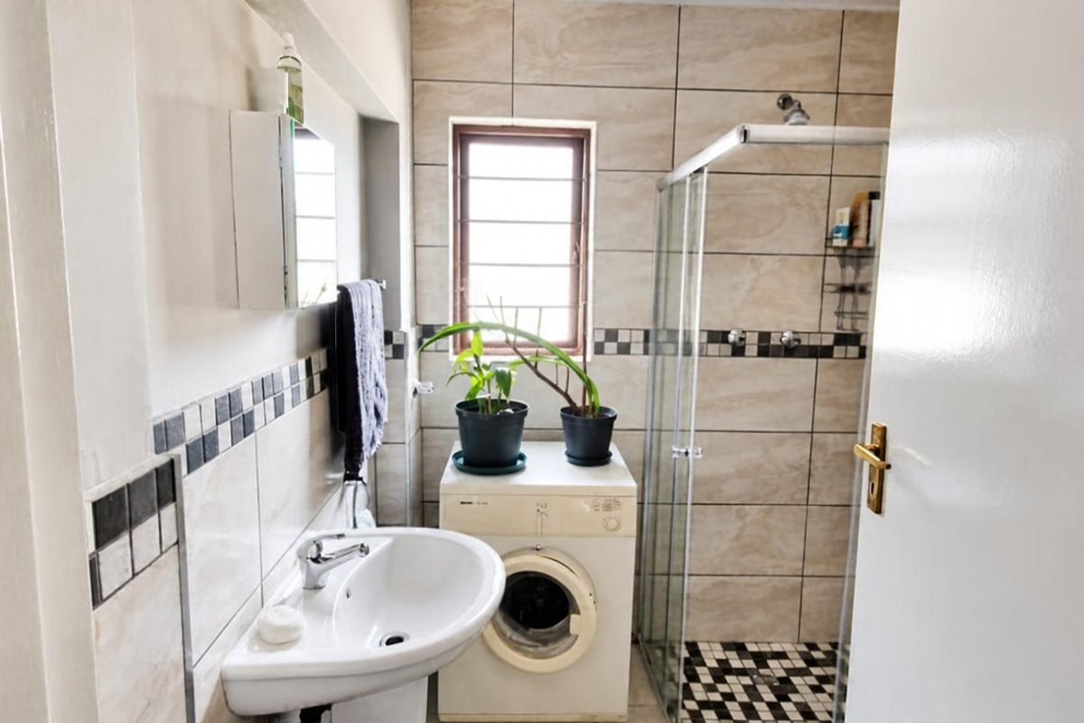A functional bathroom featuring a pedestal basin, a glass shower enclosure, and neutral wall tiling with a decorative border.