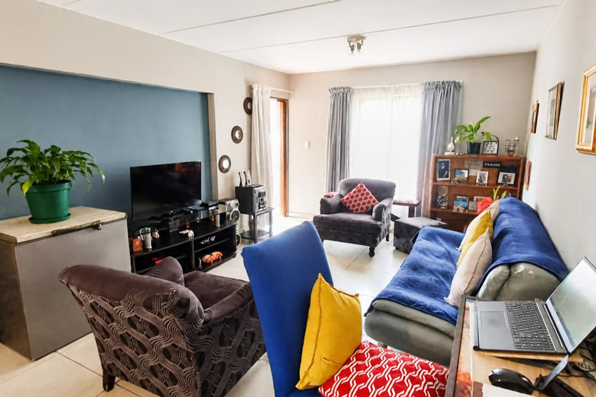 A comfortable living room featuring tiled flooring, a blue accent wall, and a sliding glass door providing natural light.