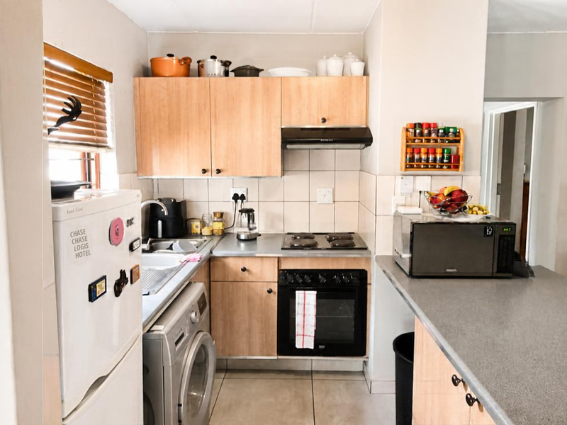 Compact kitchen featuring light wood cabinetry, laminate countertops, built-in oven and hob, tiled backsplash, and a convenient breakfast bar area.