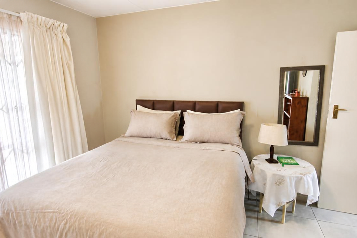 A well-lit bedroom featuring neutral wall tones, tiled flooring, and a sliding glass door providing access to the exterior.
