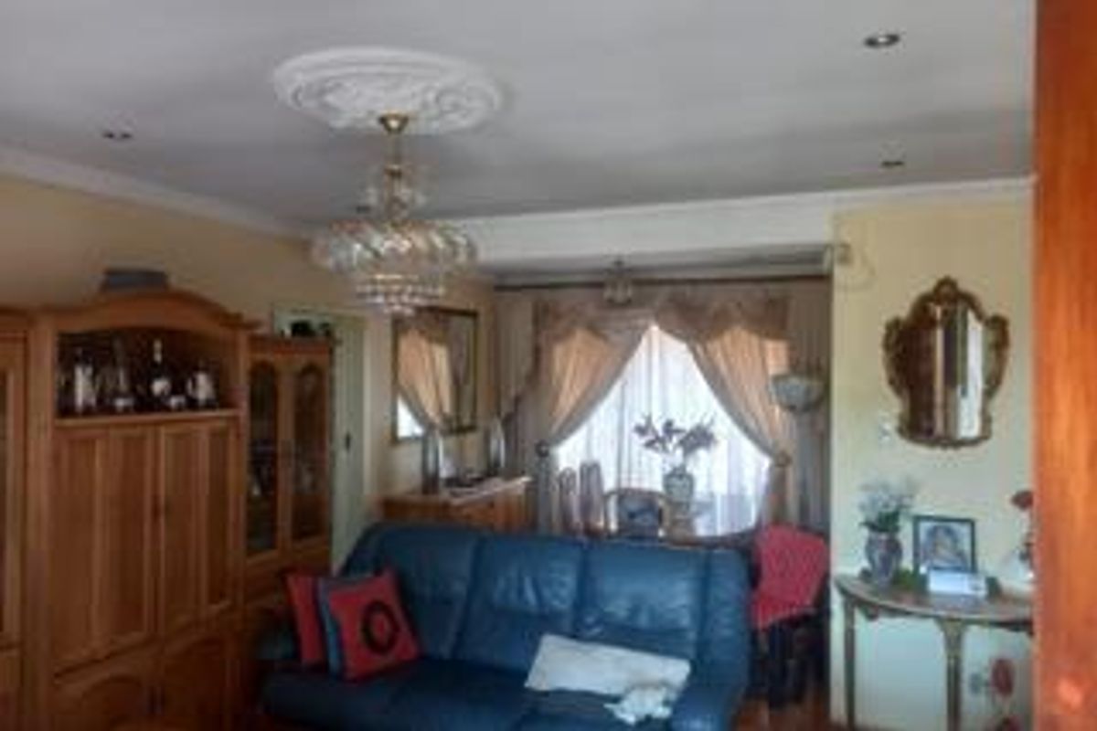 A traditional living room featuring a decorative ceiling rose, recessed lighting, and coving, with large windows dressed in curtains.
