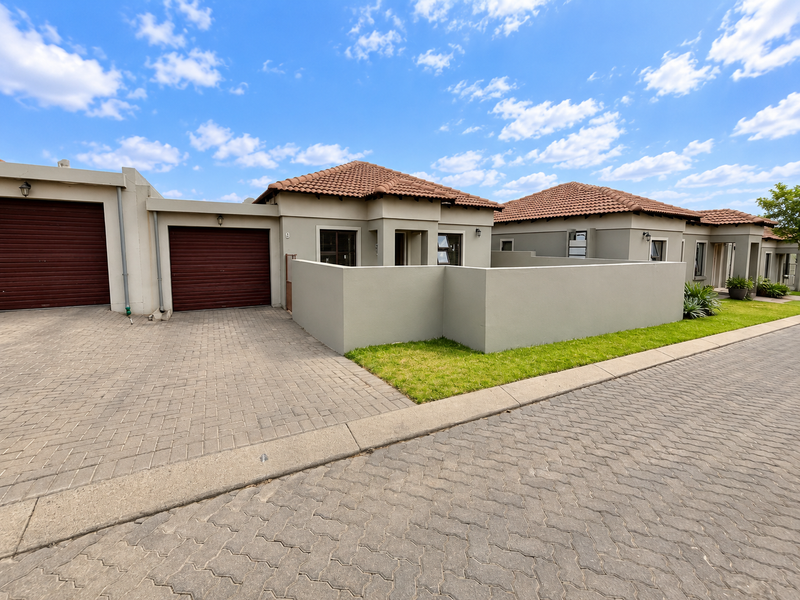 Front elevation of a townhouse featuring a paved driveway, garage access, and a private boundary wall with a small lawn area.