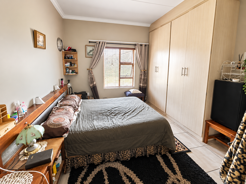 A functional bedroom featuring built-in cupboards, tiled flooring, and a window with blinds, offering a practical layout for comfortable living.