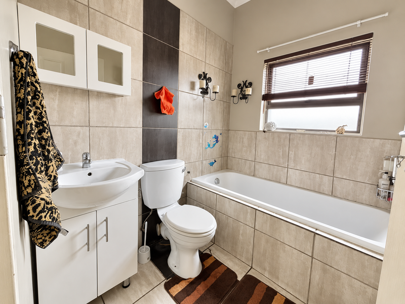 A functional bathroom featuring a vanity unit, toilet, and bathtub with neutral tiled walls and a frosted window for natural light.