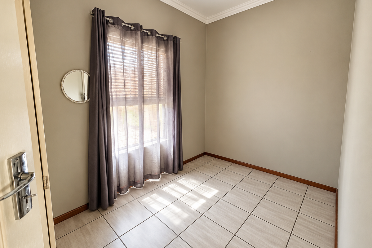 A clean, empty bedroom featuring neutral wall tones, tiled flooring, crown molding, and a window fitted with blinds and curtains.