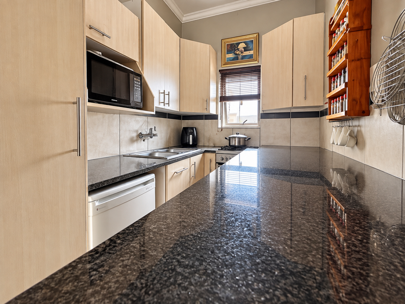 A functional kitchen featuring granite countertops, light wood cabinetry, a built-in microwave, and a gas hob with a tiled backsplash.