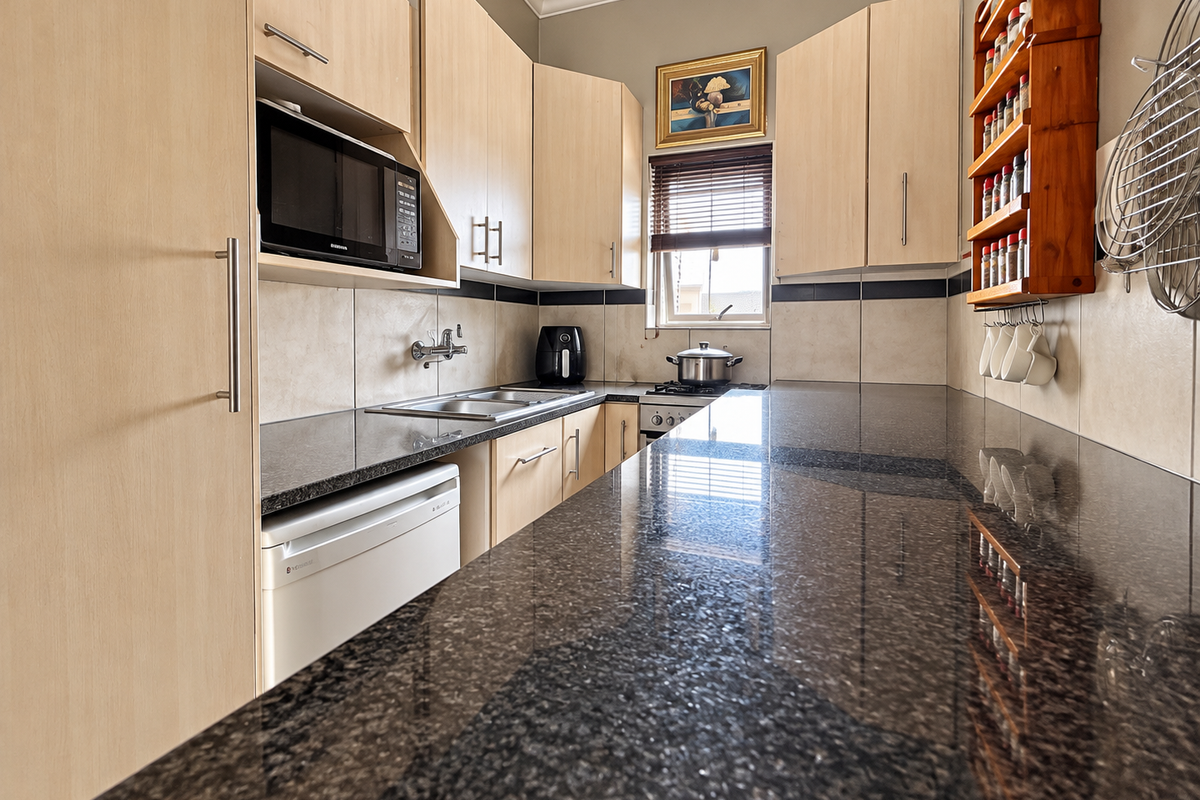 A functional kitchen featuring granite countertops, light wood cabinetry, a built-in microwave, and a gas hob with a tiled backsplash.