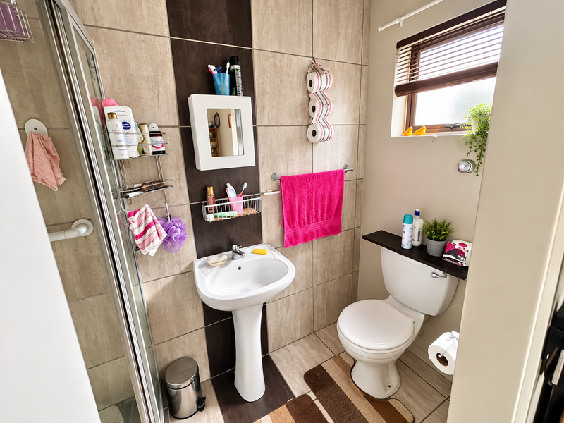 A compact, well-maintained bathroom featuring a pedestal washbasin, a toilet, and a glass-enclosed shower with neutral-toned wall and floor tiling.