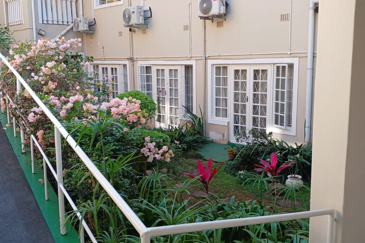 Rear exterior view of an apartment building featuring multiple french door entrances, casement windows, and a landscaped garden area with a paved walkway.
