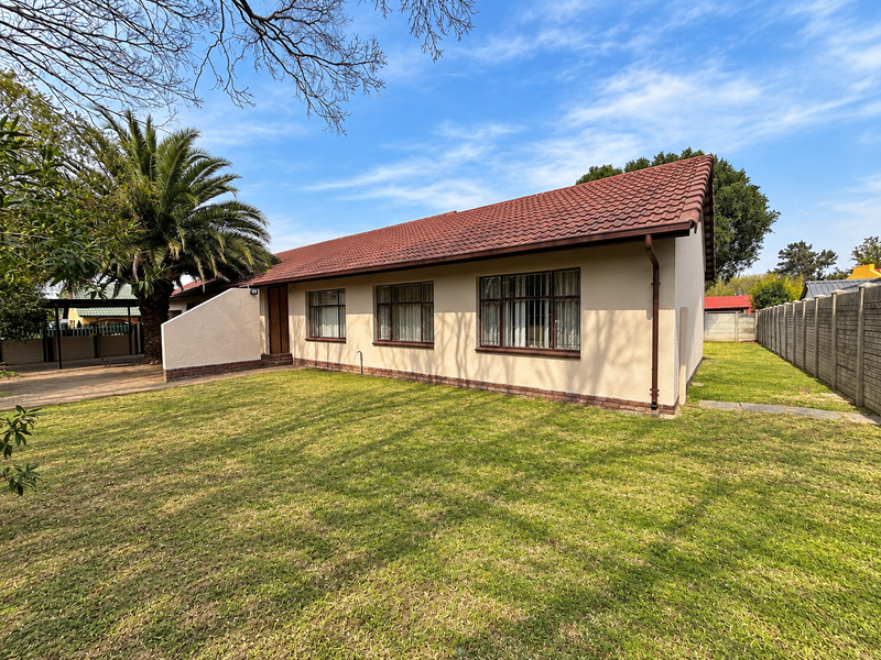 Rear view of the house featuring a tiled roof, security bars on windows, and a well-maintained lawn with a concrete boundary wall.