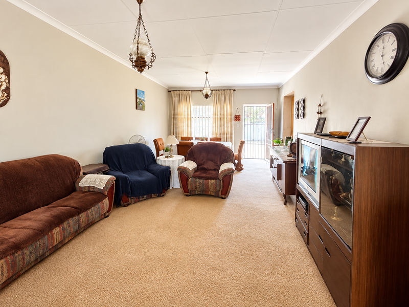 Open-plan living and dining area featuring carpeted flooring, coved ceilings, and access to the rear exterior through a security gate.