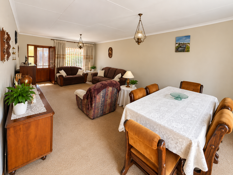 Spacious open-plan living and dining area featuring neutral wall tones, carpeted flooring, and direct access to the exterior through a timber-framed door.