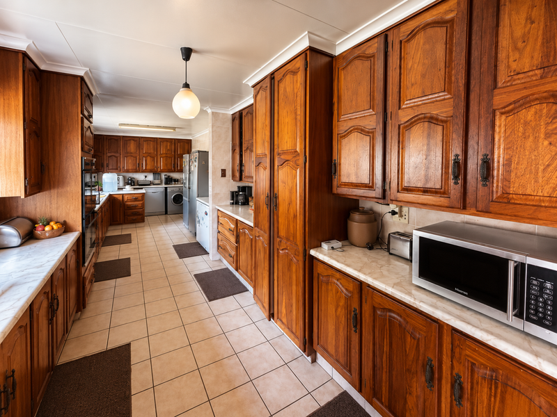 Spacious kitchen featuring extensive wooden cabinetry, marble-look countertops, tiled flooring, and integrated appliances, offering a traditional aesthetic with ample storage space.