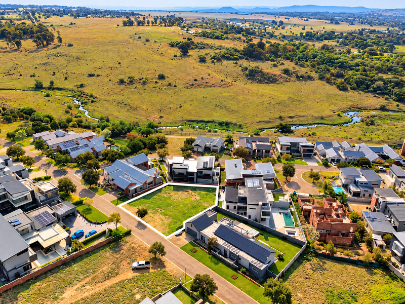 Aerial view of a vacant residential plot situated within a developed estate, featuring surrounding homes and scenic natural landscape views.