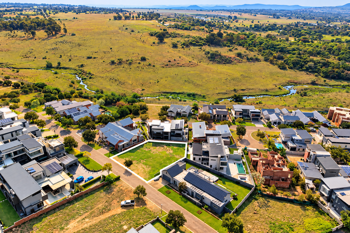 Aerial view of a vacant residential plot situated within a developed estate, featuring surrounding homes and scenic natural landscape views.