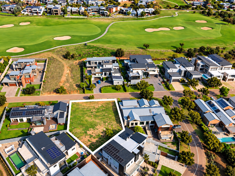 An aerial view of a vacant residential plot situated within a developed estate, adjacent to a golf course.
