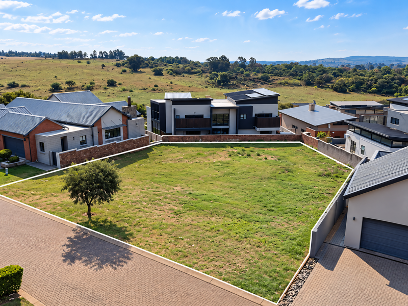 An aerial view of a vacant residential plot situated within a developed estate, featuring established boundary walls and paved access.