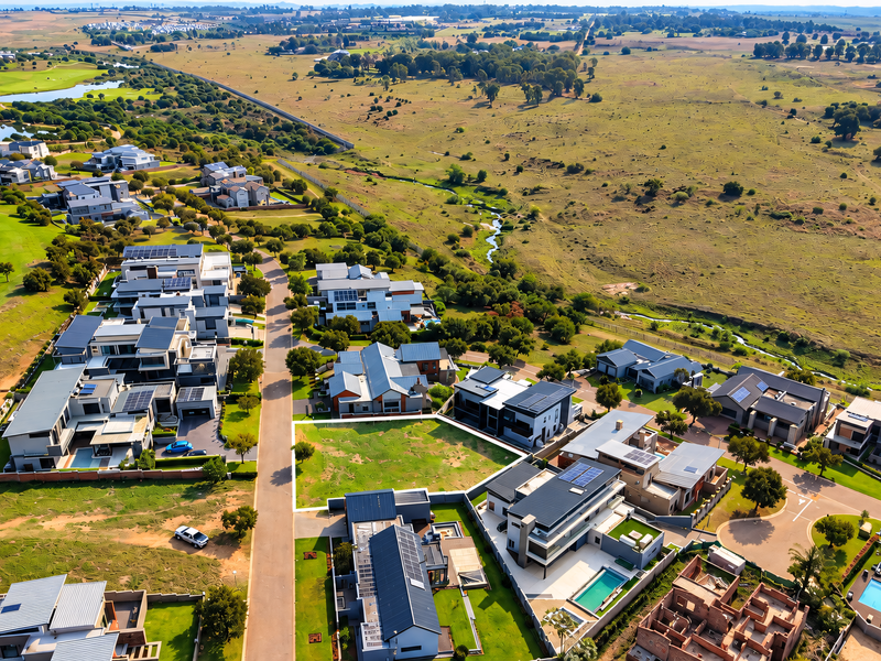 An aerial view of a modern residential estate featuring contemporary homes, swimming pools, solar installations, and proximity to a golf course and open landscape.