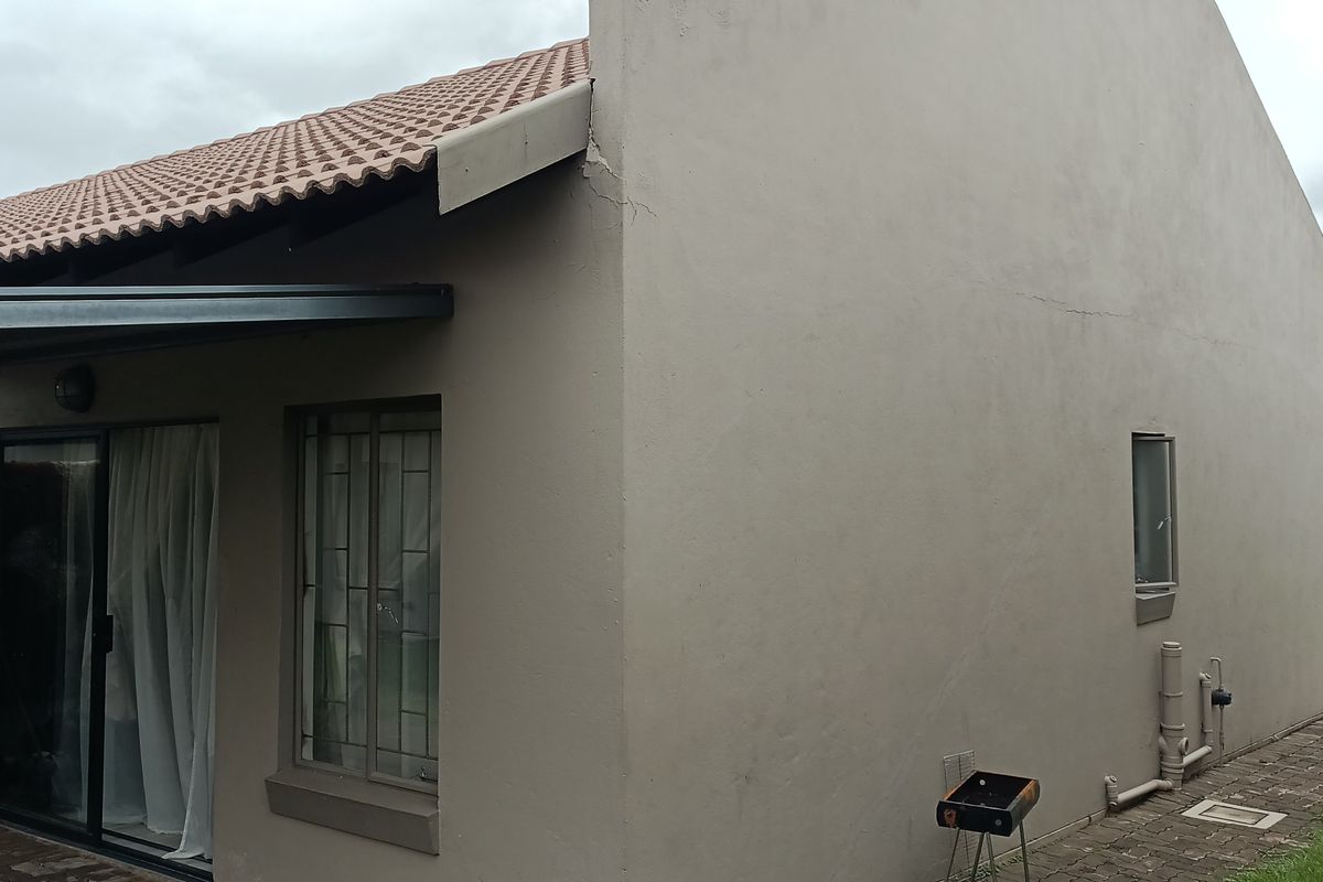 Rear exterior view of the apartment featuring a tiled roof, paved patio area, and sliding glass doors, showing visible structural cracking on the gable wall.