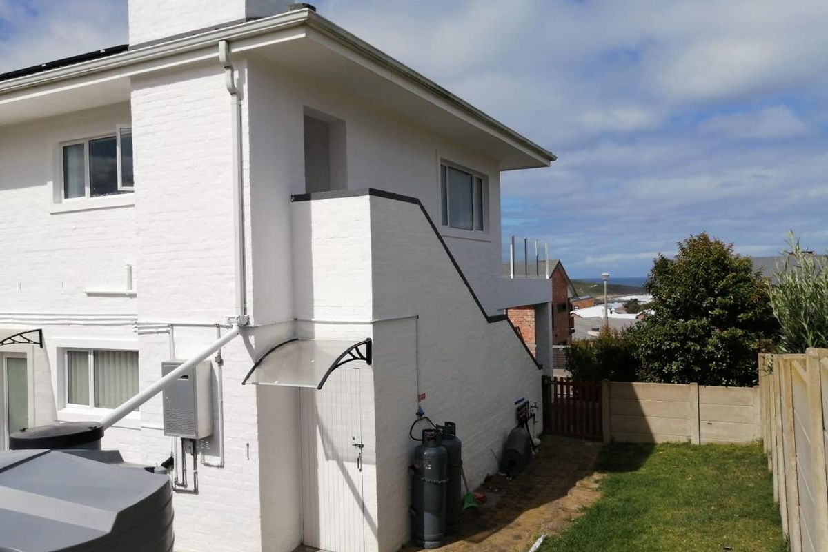 Rear exterior view of the property featuring white painted brickwork, a chimney stack, external gas cylinders, and a small paved pathway leading to the garden.