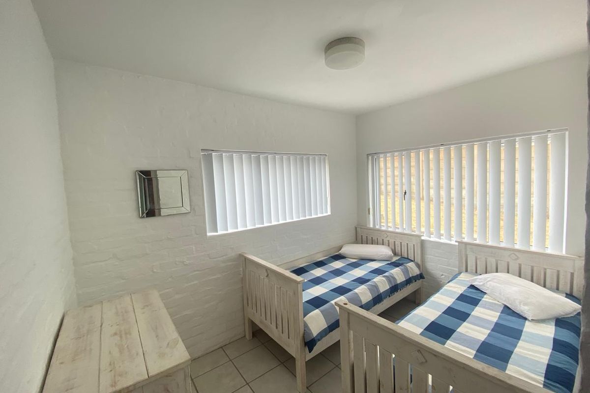 A bedroom featuring white painted brick walls, tiled flooring, and vertical blinds on the windows.