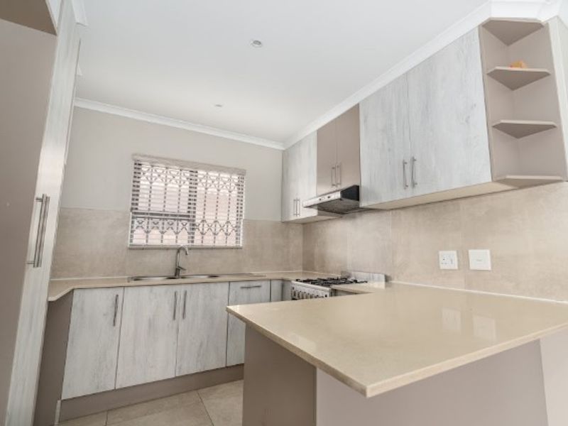 A modern, well-maintained kitchen featuring light-toned cabinetry, stone countertops, a gas stove with extractor fan, and a tiled backsplash.