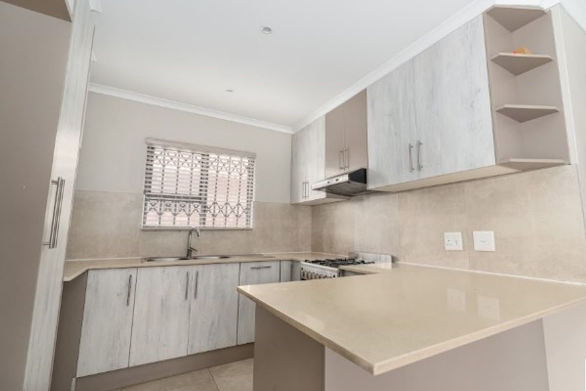 A modern, well-maintained kitchen featuring light-toned cabinetry, stone countertops, a gas stove with extractor fan, and a tiled backsplash.