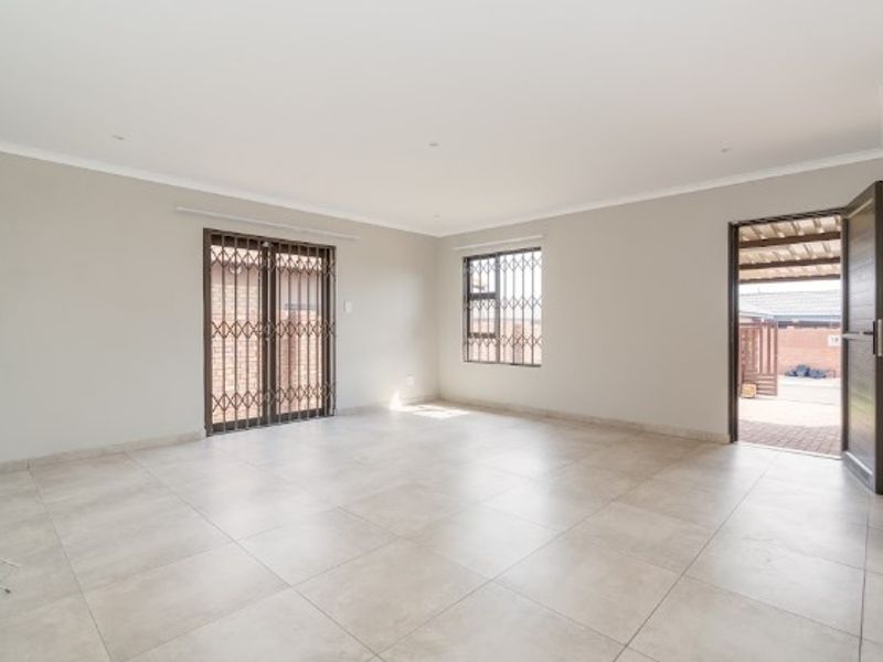 A bright, spacious, and empty living area featuring neutral tiled flooring, security gates, and direct access to an outdoor patio space.