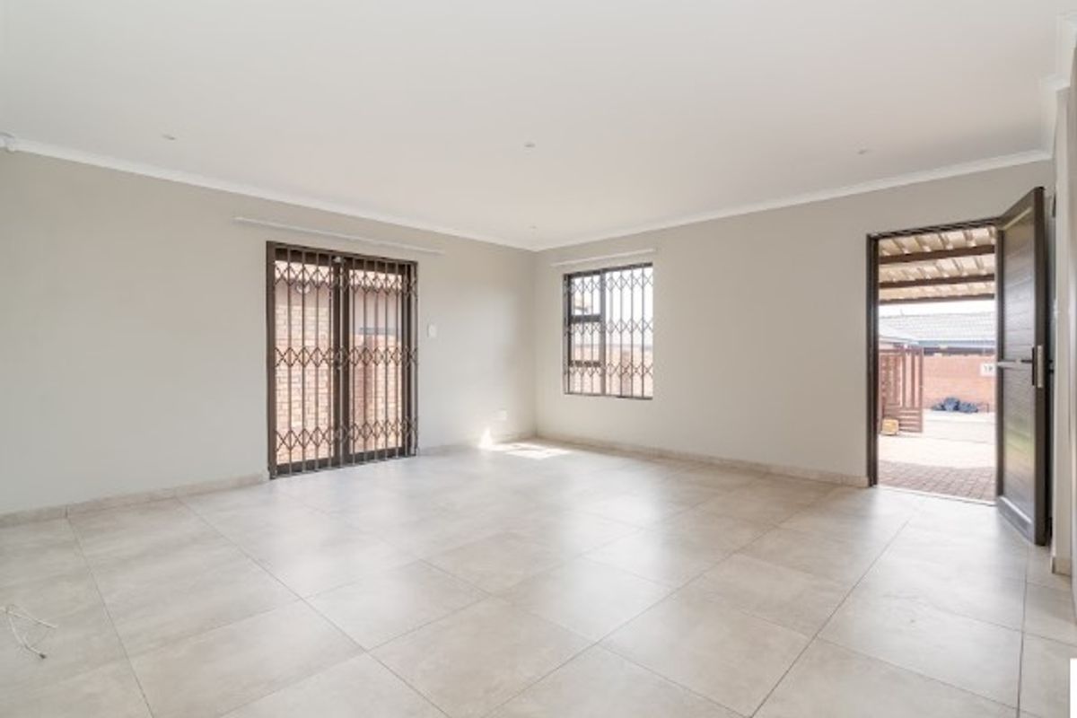 A bright, spacious, and empty living area featuring neutral tiled flooring, security gates, and direct access to an outdoor patio space.