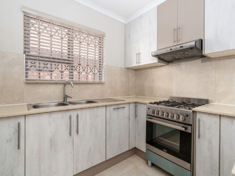 A clean and functional kitchen featuring light-toned cabinetry, a stainless steel gas stove with extractor fan, and neutral tiled finishes.