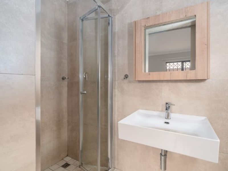 Modern bathroom featuring a glass shower enclosure, wall-mounted basin with mixer tap, and neutral floor-to-ceiling tiling.